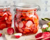 Zwei Gläser mit eingelegten Radieschen, leuchtend rot und mit schwarzen Pfefferkörnern. Frische Radieschen liegen daneben.