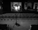 Teatr w czerni i bieli. Na scenie reflektor fresnel oświetla dekoracje, a przed nią puste rzędy siedzeń.