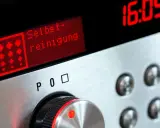 Bedienfeld eines Ofens mit rotem Display, das "Selbst-reinigung" anzeigt. Daneben die Uhrzeit 16:05.