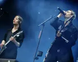 Gustaf Norén sjunger och spelar gitarr med Mando Diao på scenen, omgiven av rök och blått ljus.