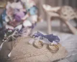 Anillos de boda sobre cojín rústico, ideas para decorar la habitación donde se viste la novia con flores y zapatos elegantes.