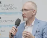 Mężczyzna w okularach i niebieskiej marynarce mówi do mikrofonu, omawiając nowe podejście do leczenia astmy, jakby to był jego własny asthma rap.