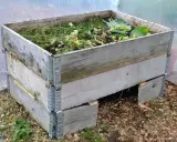 En kompost pallkrage fylld med grönt avfall och jord. Den gamla träkonstruktionen är robust och redo att omvandla trädgårdsrester till näringsrik kompost.