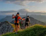Dwie osoby w sportowym stroju, z plecakami i kijkami, biegną po górskim szlaku. Idealny przykład, jak się ubrać w góry na bieg.