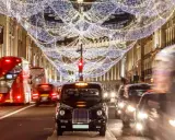 Julbelysning i London i december. Röda dubbeldäckare och taxibilar susar förbi på en livlig gata.
