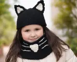 Niña sonriente con un gorro de lana con orejas de gato y bufanda a juego, tejida con agujas.