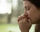 Visage pensif d'une jeune femme, mains jointes devant sa bouche, peut-être réfléchissant aux tactiques d'un manipulateur narcissique.