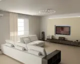 Nowoczesny salon z białymi meblami i telewizorem na ścianie. Oświetlenie niskiego sufitu tworzy przytulną atmosferę.