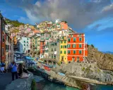 Bunte Häuserfronten der Cinque Terre Orte schmiegen sich an steile Felsen. Boote liegen im türkisfarbenen Wasser.
