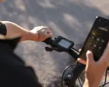 Rowerzysta trzyma telefon, na którym wyświetla się połączenie z Valerie. Obok widoczne są symbole na liczniku rowerowym, pokazujące prędkość i inne dane.