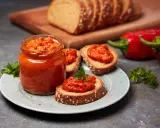 Słoik pełen ajvaru, pysznej pasty z papryki, podany z chlebem i świeżymi paprykami. Ajvar co to? To smak Bałkanów!
