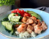 Pyszny bowl z kawałkami pieczonego lososia, świeżym ogórkiem, pomidorem i awokado na ryżu.