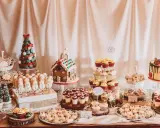 Mesa de dulces navideños con galletas de muñeco de nieve, casa de jengibre, pastel de árbol y cupcakes.