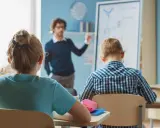 Nauczyciel mianowany zarobki - młody mężczyzna tłumaczy coś uczniom przy tablicy w jasnej sali lekcyjnej.