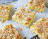 Saftiger Buttermilch Kuchen mit knusprigen Mandelblättchen und Zucker bestreut, auf Backpapier und einem Gitterrost arrangiert.