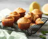 Deliciosas magdalenas caseras recién horneadas, algunas con semillas de amapola, sobre una rejilla, con rodajas de limón al fondo.
