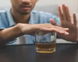 Mężczyzna odrzuca szklankę z alkoholem, symbolizując walkę z nałogiem. To obraz przymusowego leczenia alkoholika, który decyduje się na zmianę.