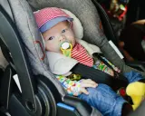 Baby mit Schnuller in Babyschale. Wann wechseln von Babyschale auf Kindersitz? Das Baby ist bereit für den nächsten Schritt.