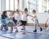 Niños aprendiendo movimientos de **deportes para niños** con una maestra en un gimnasio.
