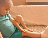 Chłopiec w turkusowej koszulce z nogą w gipsie siedzi na kanapie.