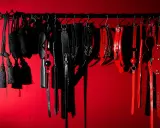 Kolekcja czarnych i czerwonych akcesoriów, takich jak bicze, kajdanki i maski, sugeruje fetysz seksualny.