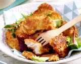 Knusprige Hähnchen-Nuggets, perfekt im Butterschmalz gebraten, auf einem Bett aus Salat. Ein Holzgabel liegt bereit.