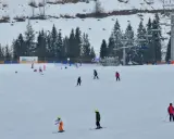 Narciarze i snowboardziści szusują po ośnieżonym stoku w Bukowinie Tatrzańskiej. W tle widać wyciąg krzesełkowy i las.