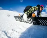 Snowboardzista w kamizelce moro i różowej czapce, zjazd na desce. Warto wiedzieć, jak dobrać buty snowboardowe, by czuć się pewnie na stoku.