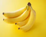 Pęczek żółtych bananów na jasnym, żółtym tle.