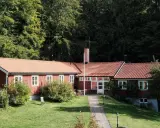 Stocklycke vandrarhem, ett rött hus med tegeltak, omgivet av grönskande träd och en välskött gräsmatta.