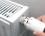 Dłoń kręci termostatem grzejnika, ustawiając temperaturę. To znak, że zbliża się czas, kiedy zaczyna się sezon grzewczy.