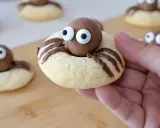 Des cookies araignée adorables avec des yeux en sucre et des pattes en chocolat, prêts à être dégustés.