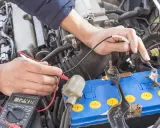 Mechanik sprawdza napięcie akumulatora za pomocą multimetru. Wynik 12.48V wskazuje na jego stan.