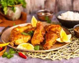 Saftiges Chicken Tandoori auf einem Teller mit Zitronenspalten und Koriander. Daneben Reis und Gewürze.