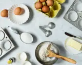 Backzutaten: Eier, Mehl, Zucker, Butter, Muffinförmchen und Messlöffel im amerikanischen Maßsystem.