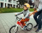 Chłopiec w kasku na rowerku 16 cali, idealnym na wiek 4-6 lat, uczy się jeździć z pomocą taty.
