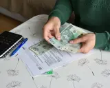 Ręce liczą banknoty 100 zł nad dokumentami ZUS. Nowe zasady zasiłków przedemerytalnych w praktyce.