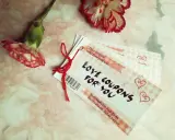 Papierowa rocznica uczczona kuponami miłości. Dwa kwiaty goździka i stosik kuponów "Love Coupons for You" na różowym tle.