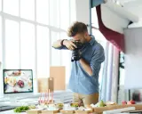Mężczyzna robi zdjęcia jedzenia. Na stole przygotowane są przekąski, napoje i owoce. To profesjonalna fotografia kulinarna.