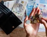 Otwarty portfel, polskie banknoty i monety w dłoni na tle dokumentów.