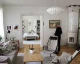 En kvinna i svart klänning står i ett rum med fransk inredningsstil. Ett sovrum syns i bakgrunden.