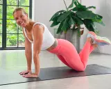 Kvinna i rosa träningskläder gör en armhävning på en yogamatta, redo för en yoga challenge.