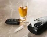 Alkomat, kluczyki samochodowe i kieliszek z alkoholem na marmurowym blacie.