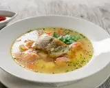 Aromatyczna zupa rybna przepis: delikatny filet rybny, kawałki łososia, ziemniaki i marchewka w bulionie, ozdobiona natką pietruszki.