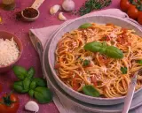 Ein Teller Spaghetti Napoli mit Tomatensauce, Basilikum und Parmesan. Daneben Zutaten wie Tomaten, Knoblauch und Olivenöl.
