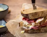 Ein üppiges Pastrami-Sandwich mit Röstbrot, serviert mit Beilagen wie Krautsalat und Senf.