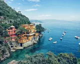 Bunte Villen am Hang über dem türkisfarbenen Meer bei Portofino, Italien. Boote schaukeln sanft auf dem Wasser.