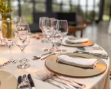 Une table élégamment dressée pour un repas, avec la position des verres à la française. Des assiettes, serviettes et couverts sont prêts.