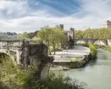 Un ponte rotto, con archi antichi e vegetazione rigogliosa, domina un fiume serpeggiante a Roma.
