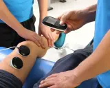 Rehabilitacja: fizjoterapeuta z urządzeniem do elektroterapii przy nodze pacjenta.